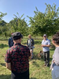 A Group Of People, Include The Fabulous 413's Monte Belmonte, Listen As Jono Neiger Talks About Regenerative Agriculture In The Fields Of Big River Chestnuts