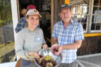 Ellena Baum And Jono Neiger Smiling And Looking At Camera And Holding Handfuls Of Fresh Chestnuts